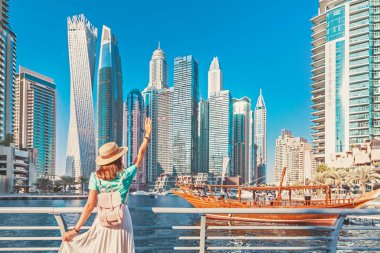 Cheerful asian traveler girl walking on a promenade in Dubai Marina district. Travel destinations and tourist lifestyle in UAE