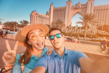 A couple in love arrived for their honeymoon in Dubai and takes a selfie in front of their hotel on the island of palm Jumeirah