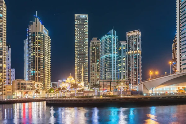 27 de novembro de 2019, Emirados Árabes Unidos, Dubai: luzes multicoloridas da cidade noturna no distrito da Marina do Dubai e mesquita iluminada com minaretes. Cidade e religião modernas — Fotografia de Stock