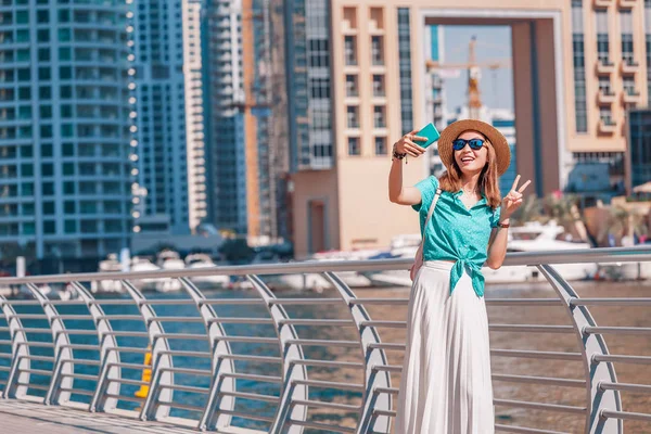 Menina asiática feliz tirando foto selfie em um smartphone enquanto caminha em um passeio marítimo no distrito de Dubai Marina. Viagens e estilo de vida em Emirados Árabes Unidos — Fotografia de Stock