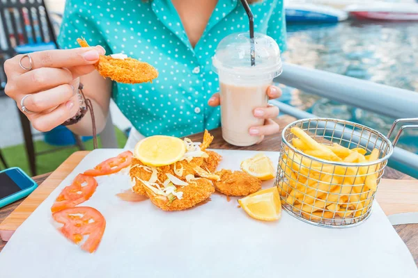 A girl eats prawns in batter and French fries on the terrace of a sea cafe — Stock Photo, Image