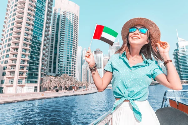 Asian girl waving UAE flag on a boat cruise ship with skyscrapers of Marina port in Dubai in the background — Stok fotoğraf