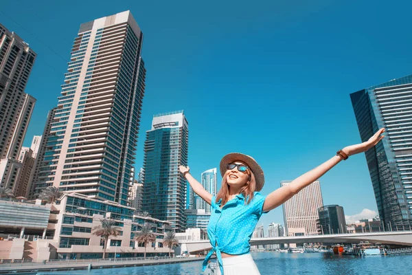 Счастливая туристка поднимает руки и наслаждается потрясающим видом на небоскребы в районе причала Дубая. Путешествие в Объединенные Арабские Эмираты — стоковое фото