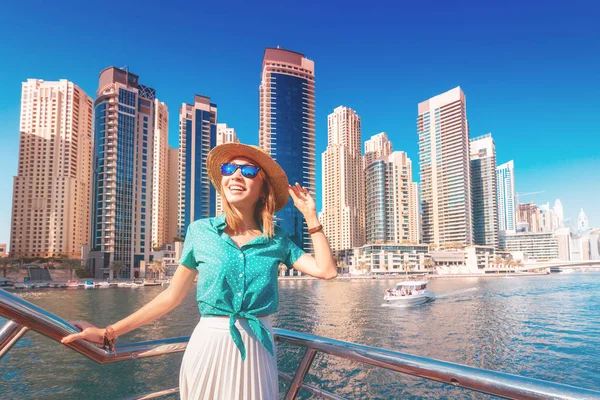 Cheerful girl traveler on a ferry boat sailing through Dubai Marina port among huge skyscrapers. Concept of tourism in the UAE