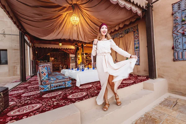 Mujer feliz viajera vistiendo vestido y turbante caminando por las calles de una antigua ciudad o pueblo árabe en medio del desierto. Concepto de turismo y aventura solo — Foto de Stock