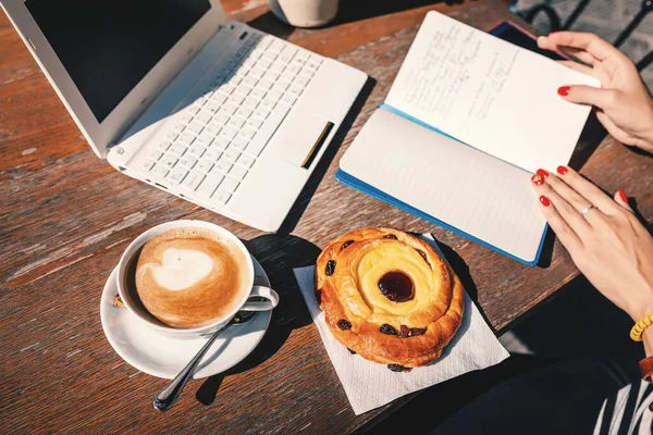 writer or a representative of another creative profession works at a laptop and makes notes in a notebook during Breakfast in a cafe