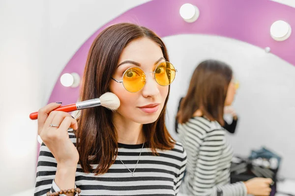 Asian girl puts on makeup and poses with a brush near a large pink mirror at home