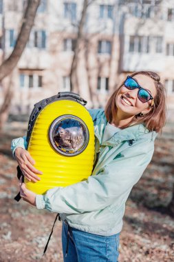 Mutlu kız evcil hayvan sahibi kedisiyle parkta yürürken gülümsüyor. Arkadaşlık ve kedi taşıyıcısı. Yaşam tarzı ve eğlence.