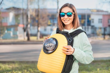 Mutlu kız evcil hayvan sahibi kedisiyle parkta yürürken gülümsüyor. Arkadaşlık ve kedi taşıyıcısı. Yaşam tarzı ve eğlence.