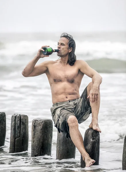 Человек, сидящий у моря и пьющий алкоголь — стоковое фото