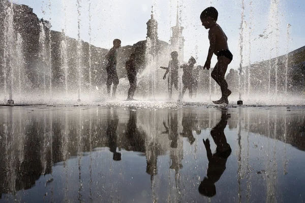 Niños felices jugando en una fuente de agua en un día caluroso —  Fotos de Stock