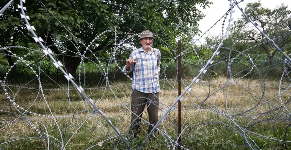 Oude man op lokale stand in de buurt van prikkeldraad — Stockfoto