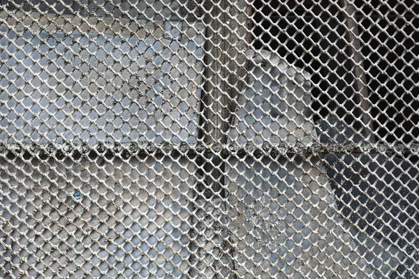 Old metal mesh on a broken window. Broken glass behind a rusty metal mesh