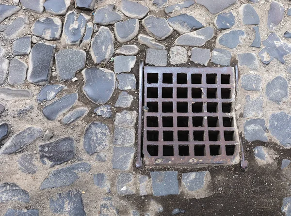 排水システムの古い鉄格子は舗装石で舗装道路に孵化します — ストック写真