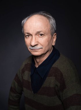 Karanlık bir arka planda yaşlı ve yorgun bir adamın stüdyo portresi. Şüpheci görünüyor.