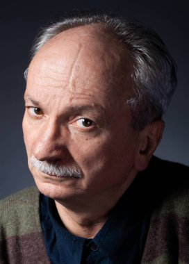 Karanlık bir arka planda yaşlı ve yorgun bir adamın stüdyo portresi. Şüpheci görünüyor.