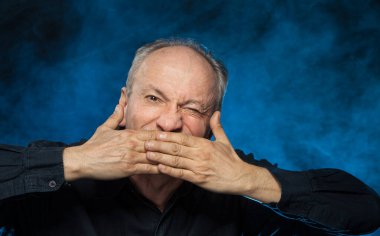 Yaşlı maço adam. Yaşlı bir adam avuçlarıyla ağzını kapatır. Stüdyonun karanlık arka planında yaşlı duygusal bir adamın portresi.