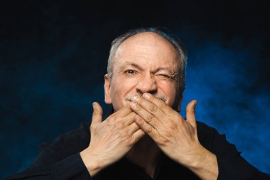 Yaşlı maço adam. Yaşlı bir adam avuçlarıyla ağzını kapatır. Stüdyonun karanlık arka planında yaşlı duygusal bir adamın portresi.