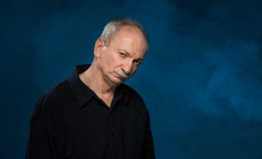 Yaşlı maço adam. Yorgun yaşlı adam. Stüdyonun karanlık arka planında yaşlı duygusal bir adamın portresi.