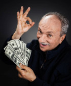 Starší pán drží hromadu peněz. Portrét vzrušeného starého muže. Šťastný stařec držící dolarové bankovky.