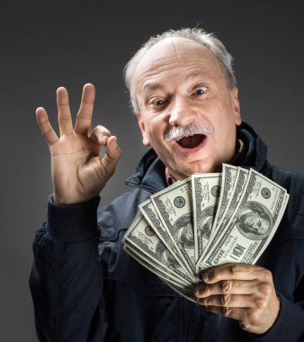 Kıdemli beyefendi bir tomar para tutuyor. Heyecanlı yaşlı bir adamın portresi. Dolarlık banknotlar tutan mutlu yaşlı adam..
