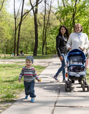 Kyiv, Ukrayna - Mayıs. 01, 2017: Mutlu aile parkta yürüyor. Bebek arabalı büyükanne, kızı ve parktaki bir sokakta karahindiba taşıyan küçük bir çocuk.