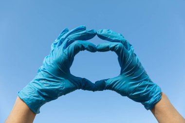 Lateksten yapılmış kalp, doktor için nitril tıbbi eldiven ve mavi gökyüzü arka planında hemşire koruması.