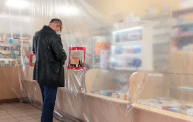 Bucha, Ukrayna - Nisan. 24, 2020: Eczanelerdeki karantina sırasında filmin olduğu bölgelerin sınırlandırılması. Müşteri, Bucha 'nın Kyiv bölgesinde plastik filmle korunan bir eczaneden ilaç alıyor.