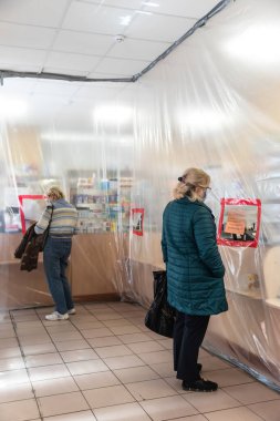 Bucha, Ukrayna - Nisan. 24, 2020: Eczanelerdeki karantina sırasında filmin olduğu bölgelerin sınırlandırılması. Müşteri, Bucha 'nın Kyiv bölgesinde plastik filmle korunan bir eczaneden ilaç alıyor.