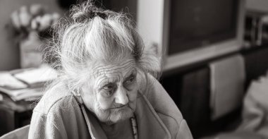 Yaşlılık konsepti. Çok yaşlı ve yorgun bir kadının portresi. Evinin yatak odasındaki pencerenin yanında kırışık bir kadın. Üzgün ve bunalımlı yaşlı kadın yalnız