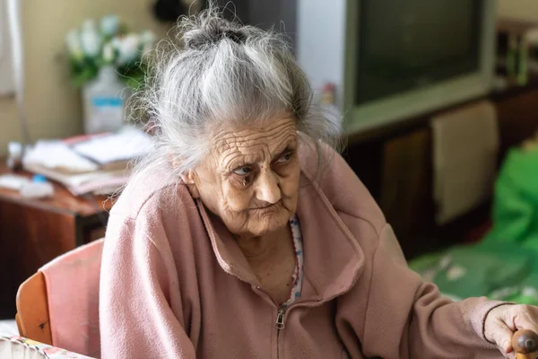Old age concept. Portrait of a very old and tired of life wrinkled woman near the window in the bedroom of her house. Sad and depressed older woman alone