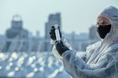 Coronavirus Covid 19, bilim adamının elindeki örnek tüpte enfekte olmuş. Şehrin önündeki koruyucu giysi doktoru..