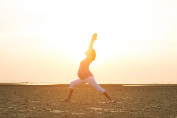 Madre embarazada realizando yoga en la playa — Foto de Stock