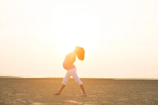 Hamile anne kumsalda Yoga gerçekleştirme — Stok fotoğraf