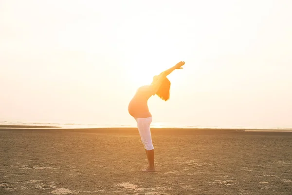 Hamile anne kumsalda Yoga gerçekleştirme — Stok fotoğraf