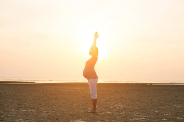 Hamile anne kumsalda Yoga gerçekleştirme — Stok fotoğraf