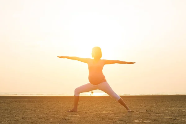 Hamile anne kumsalda Yoga gerçekleştirme — Stok fotoğraf