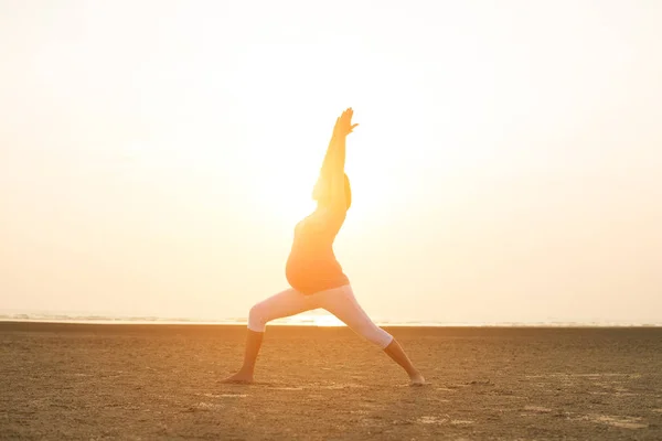 Hamile anne kumsalda Yoga gerçekleştirme — Stok fotoğraf