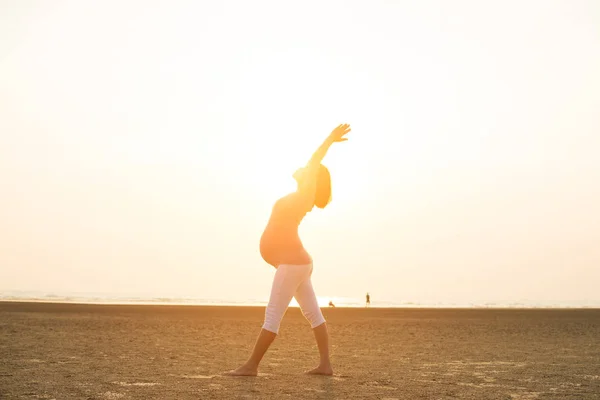 Hamile anne kumsalda Yoga gerçekleştirme — Stok fotoğraf