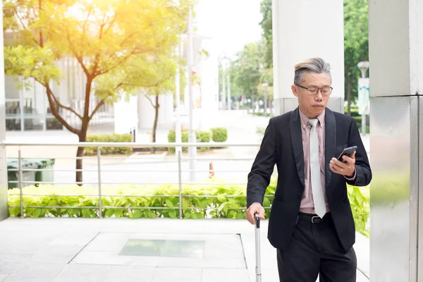 资深亚洲商人用智能手机携带行李 — 图库照片