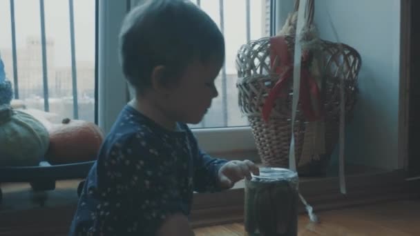 Pequeño bebé sentado en la cocina cerca de la ventana, luego coronando debajo de la mesa — Vídeo de stock