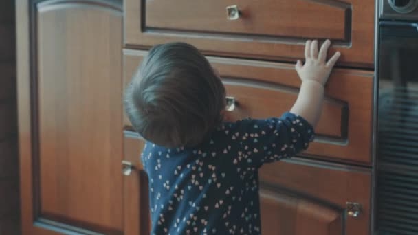 Kleine baby permanent in de buurt van de kast, dan zitten op de vloer — Stockvideo