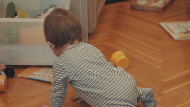Bambino piccolo che gioca con la pentola arancione, agitando le mani e crowling — Video Stock