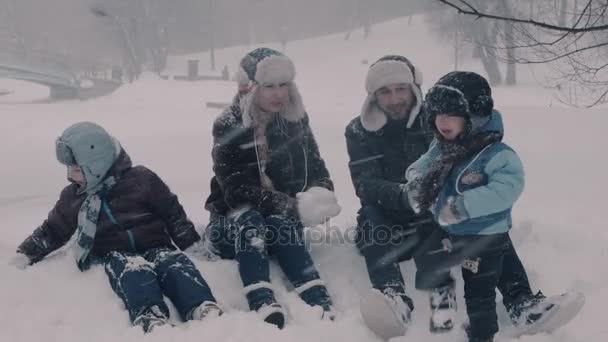 Famille assise sur la neige. Deux garçons et leurs parents. Maman fait des boules de neige . — Video