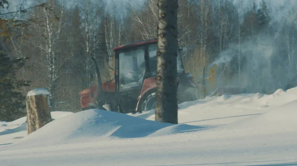 Trator removendo neve da estrada de inverno na floresta — Fotografia de Stock