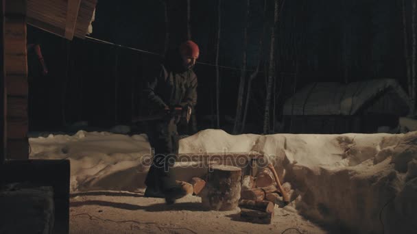 Un joven cortando leña en el patio. Noche de invierno . — Vídeos de Stock