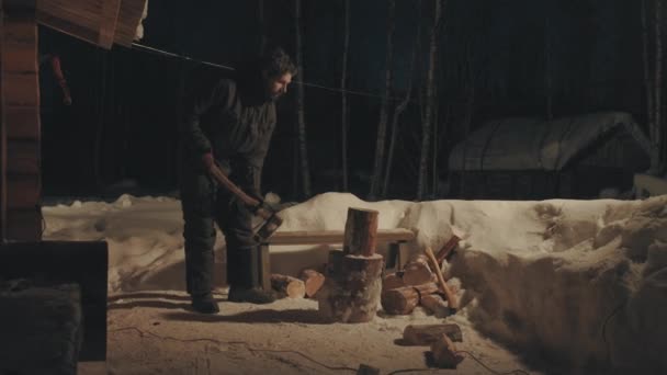 Jonge man hakken van hout in de tuin. Winteravond. — Stockvideo