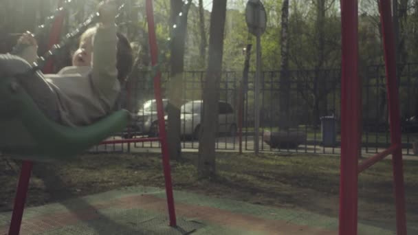 Mamá balanceando a un niño en un columpio en el patio — Vídeo de stock