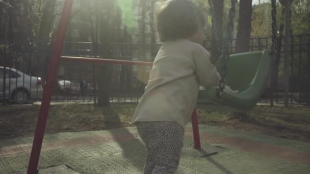 Un niño cerca de un columpio en el patio — Vídeos de Stock