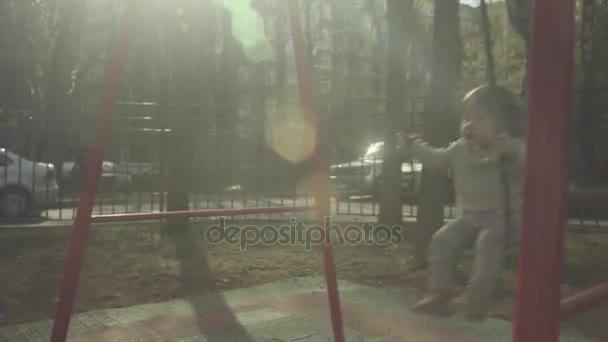 Mamá balanceando a un niño en un columpio en el patio — Vídeo de stock